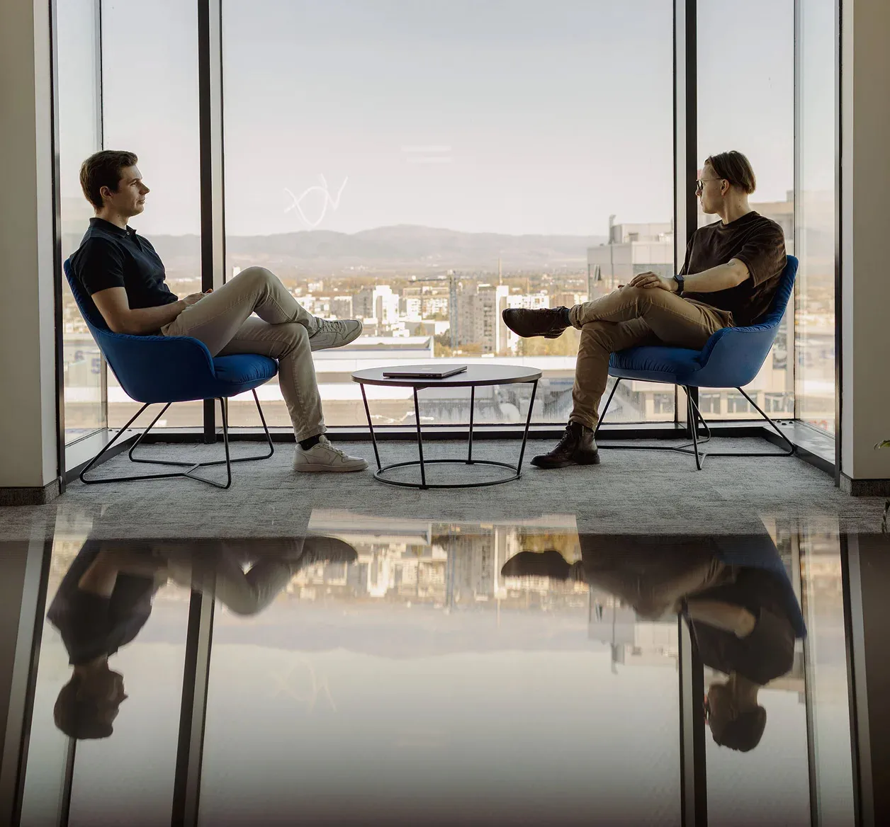 Two men sitting across each other looking out the office window