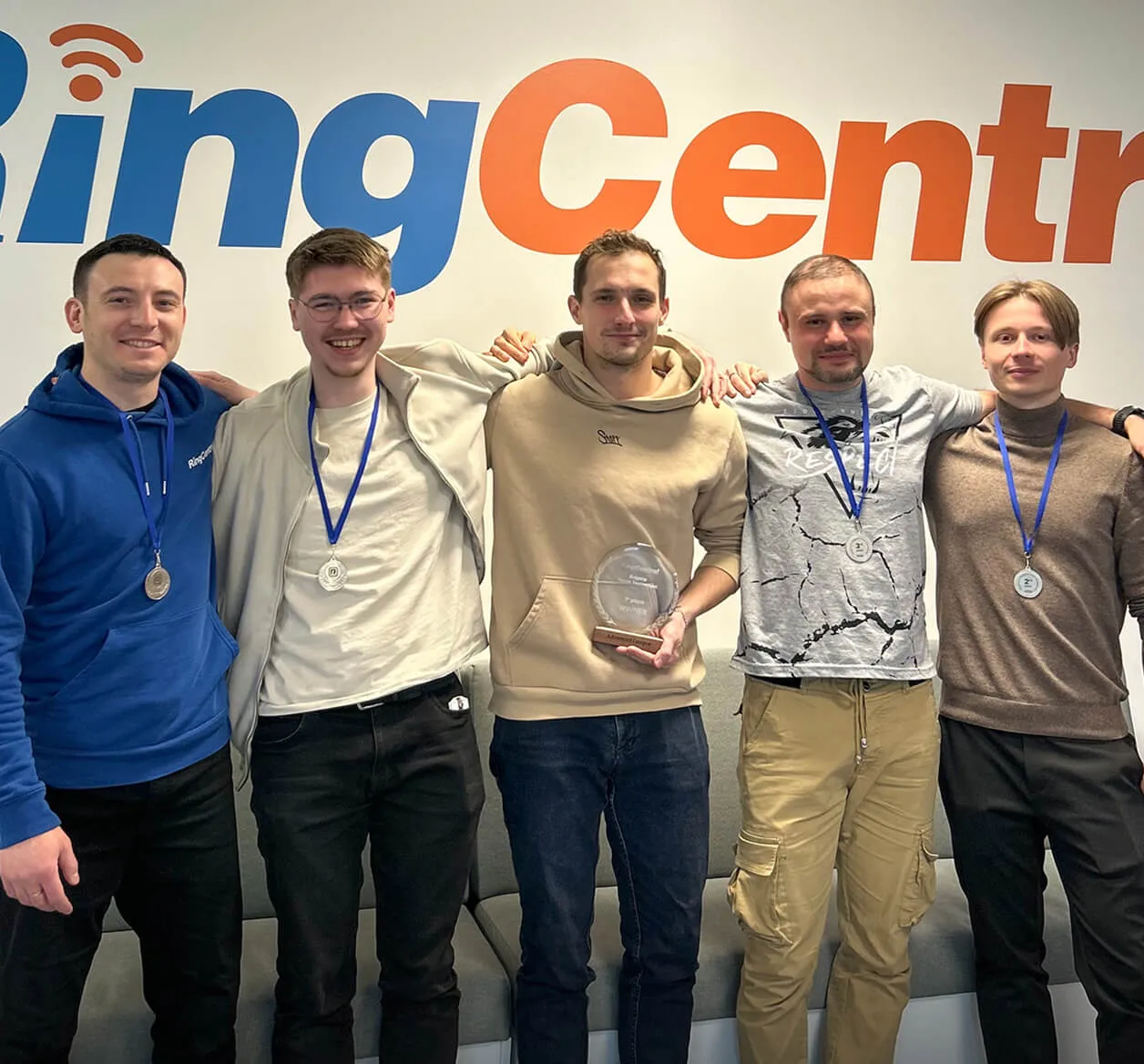 Five RingCentral employees wearing a medal with the center guy holding a trophy