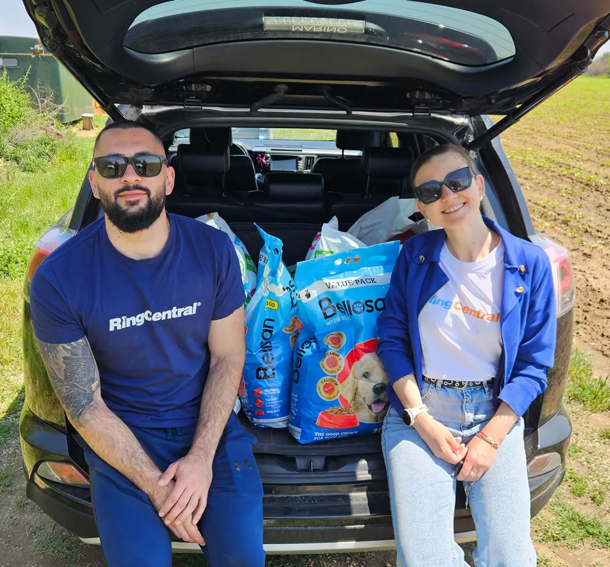 Two RingCentral employees at sitting on an open car trunk filled wih sacks of dog food