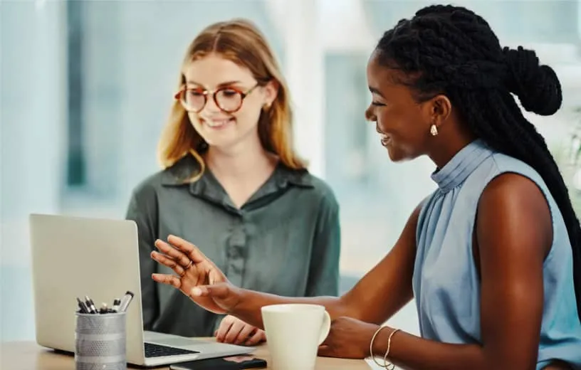 Two female colleagues discuss about customer relationships strategies in front of a laptop