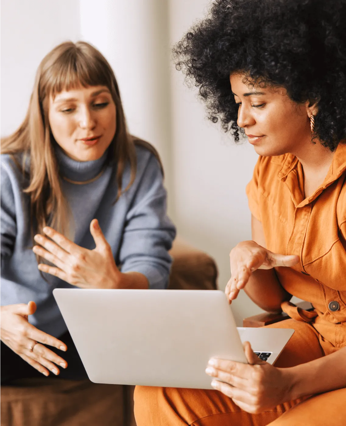 Two female coworkers discussing and viewing a project on a laptop