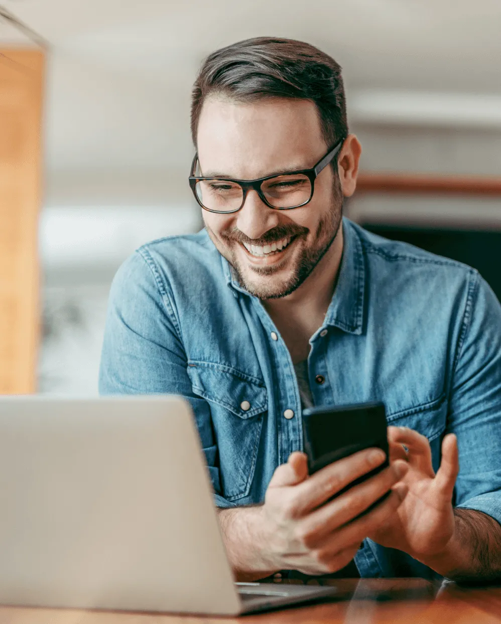 Un hombre que sostiene su teléfono móvil mientras mira su computadora portátil
