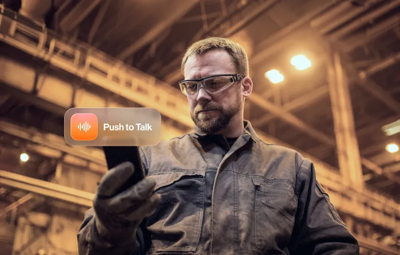 Worker in an industrial setting using a smartphone with the Push to Talk feature highlighted.