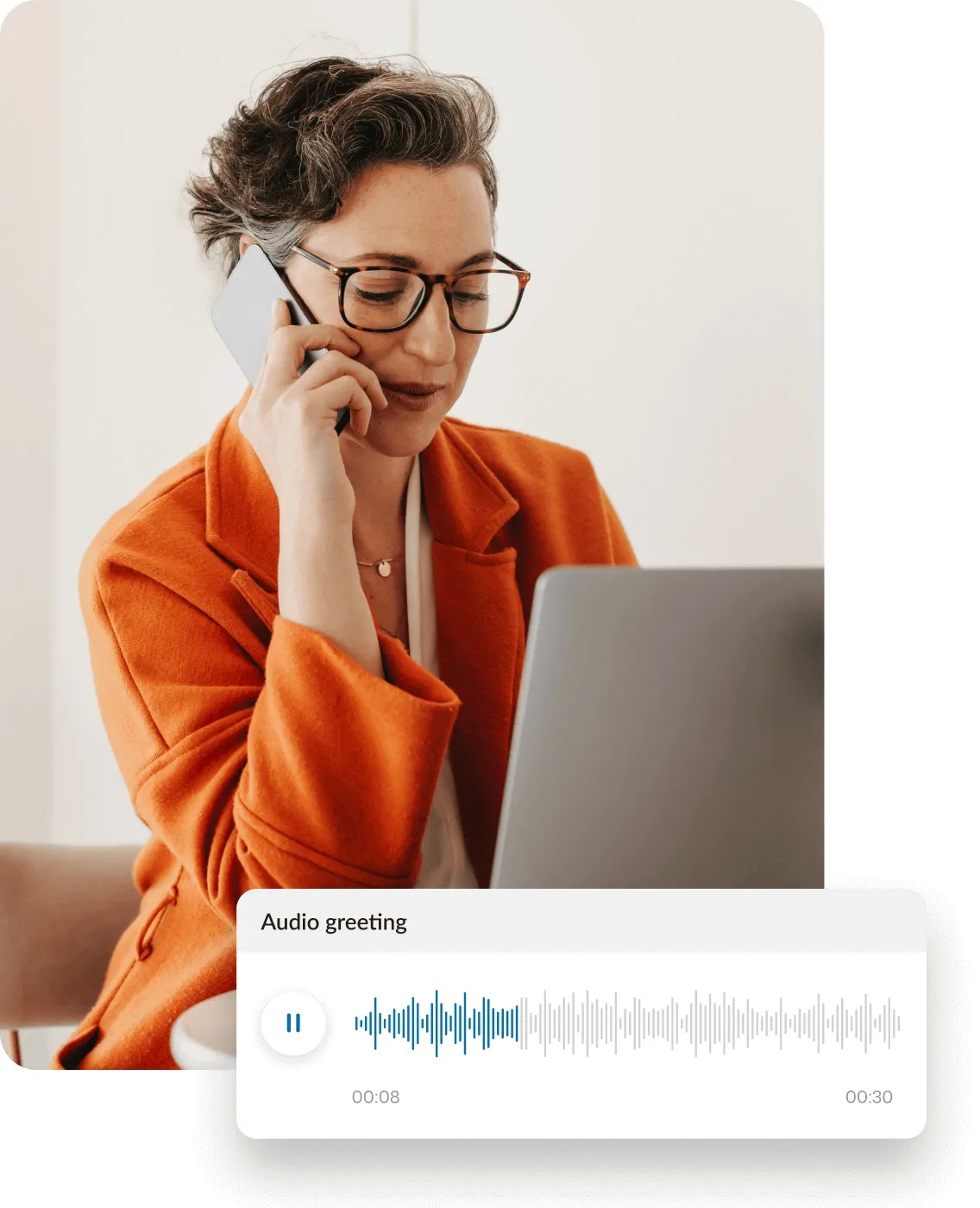 A woman records a company phone greeting on her phone while working on a laptop