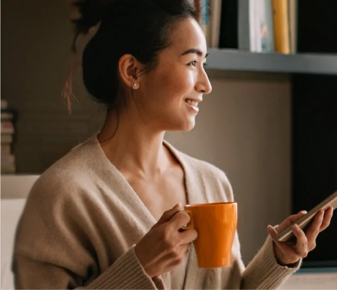 A woman holding a cup of coffee and a mobile phone