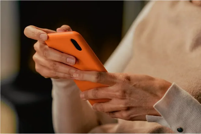 Hands holding an orange mobile phone