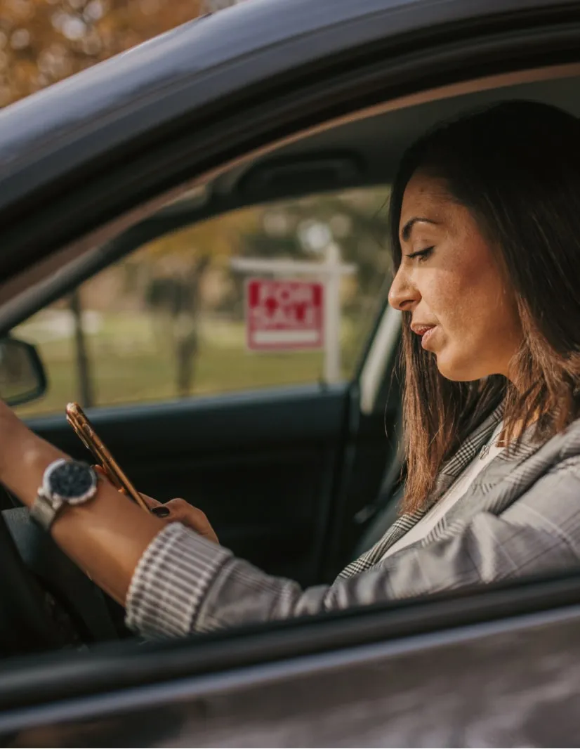 A female executive working on her phone while on a parked car
