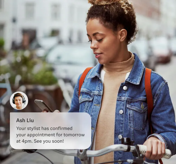 A woman receives a Business SMS notification on her phone regarding her appointment with a stylist