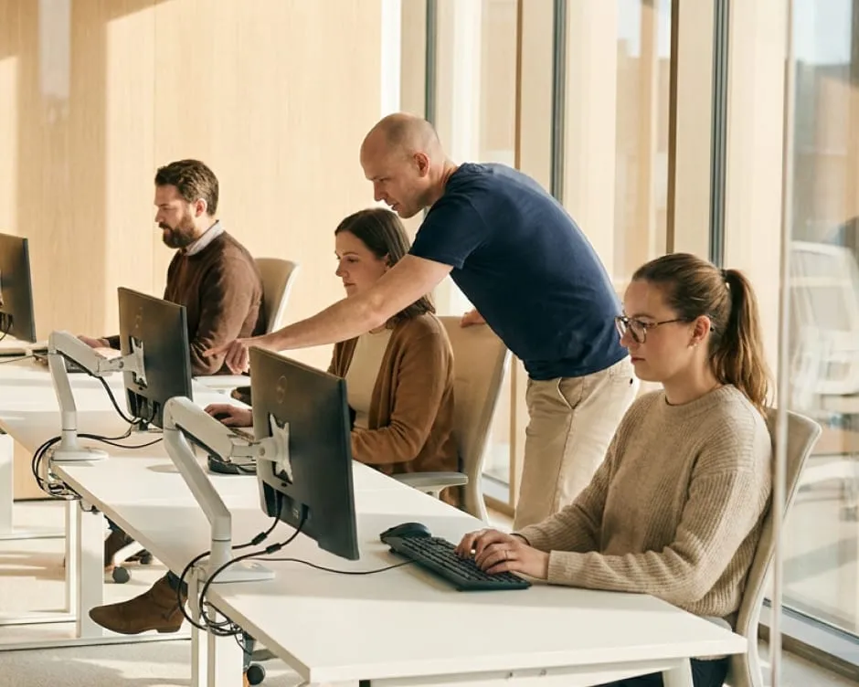 A team of professionals working on desktop computers, collaborating in an office environment.