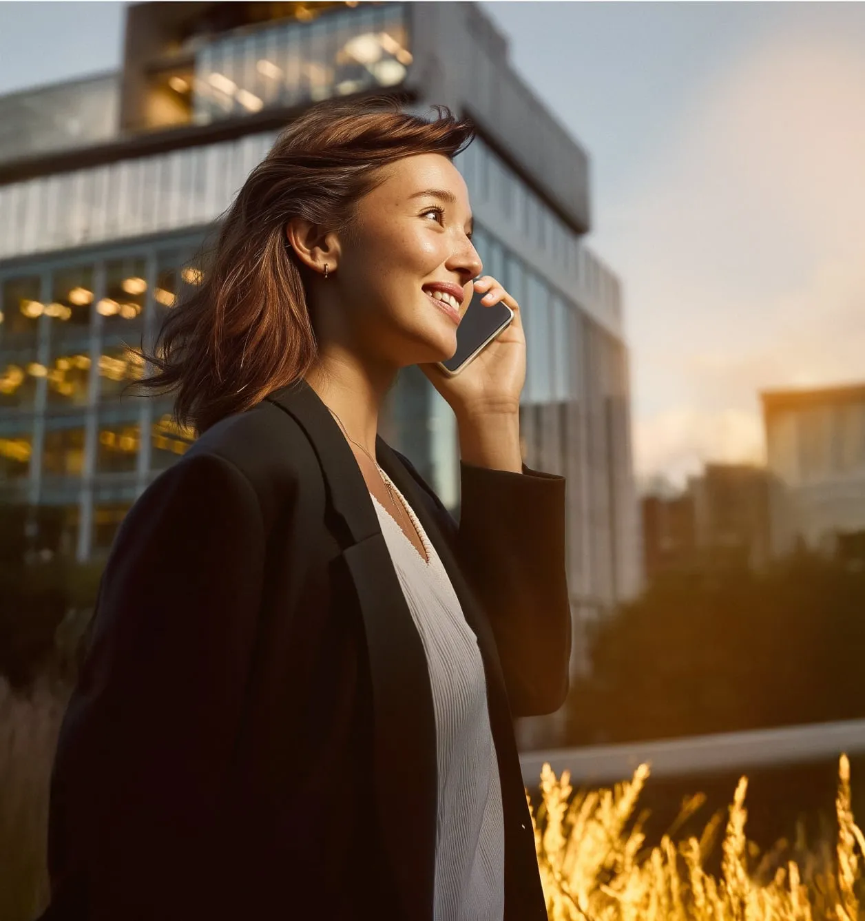 A woman is walking outside and smiling while holding her mobile phone.