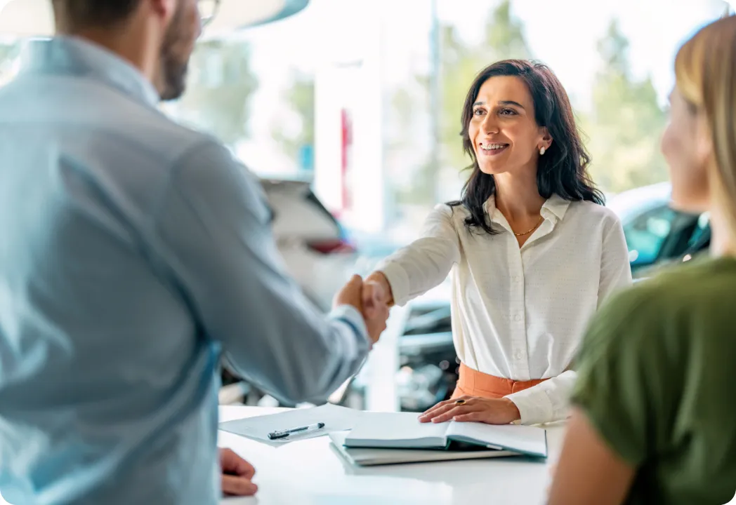 A woman and a man shake hands inside a car dealership, signifying a successful negotiation or agreement.