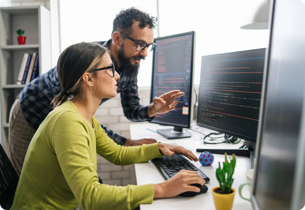 A man and woman collaborating on a computer, focused on their work in a modern office setting.