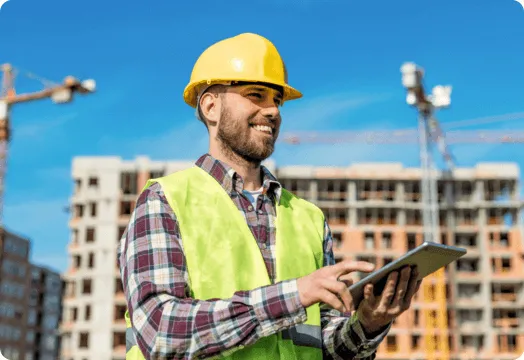 1. A man wearing a hard hat and safety vest is holding a tablet computer on a construction site.