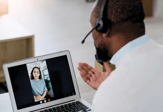 A man with a headset is engaged in a conversation while using a laptop.