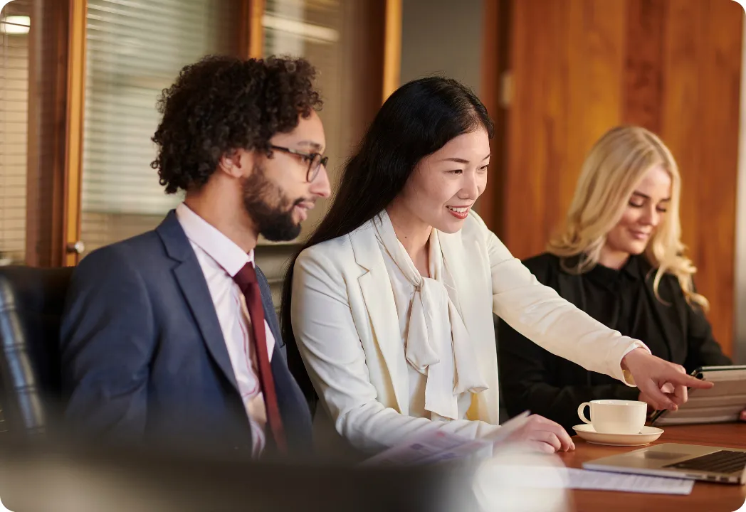 Three business professionals seated at a table, collaborating over a laptop during a meeting.
